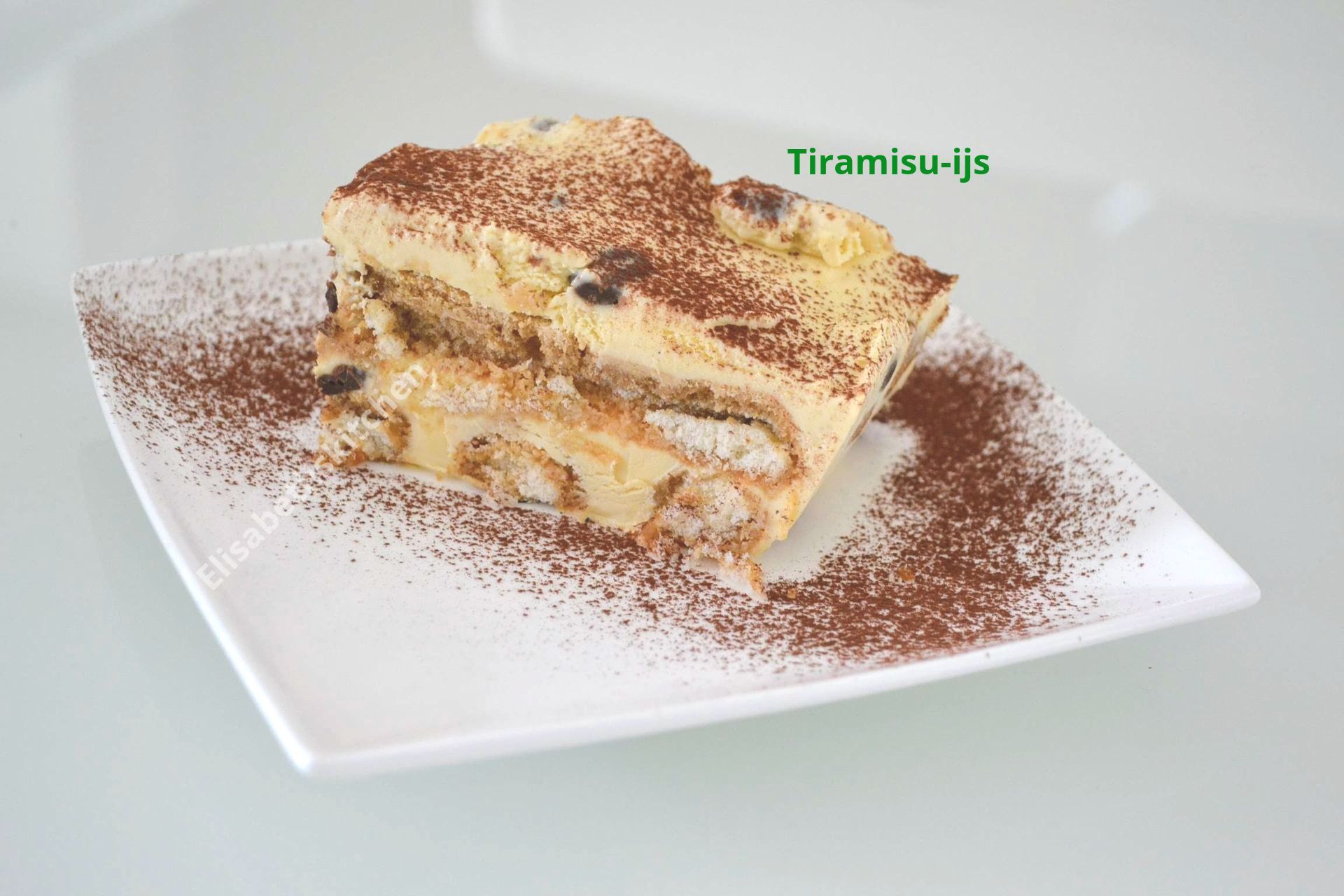 Tiramisu-dessert op een wit vierkant bord, bestrooid met cacaopoeder, met lichtgekleurde laagjes.