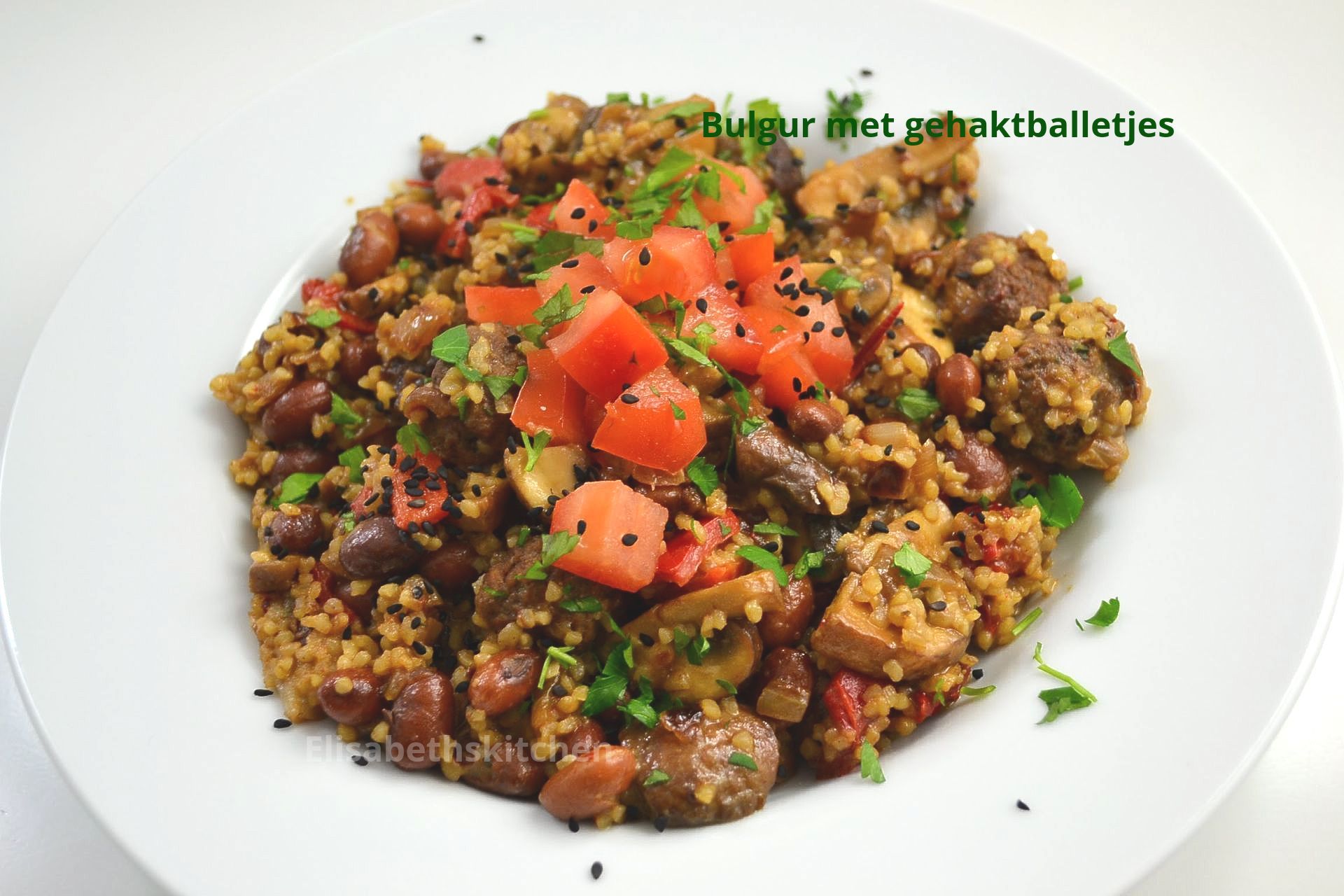 Bulgurgerecht met gehaktballetjes, tomaten, bonen en kruiden, geserveerd op een wit bord.
