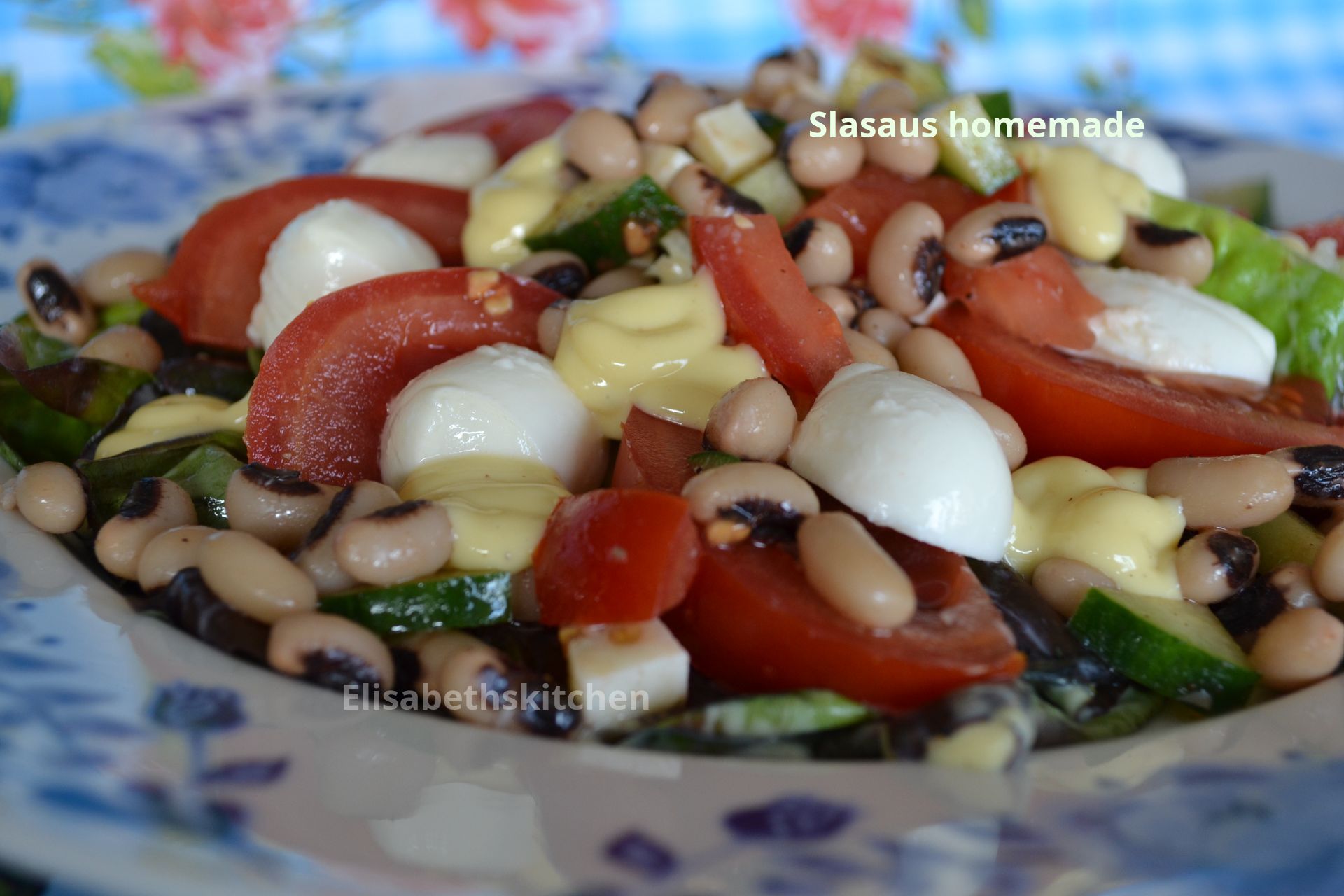 Salade met zwarte bonen, tomaten, mozzarella, komkommer en dressing op een bord met bloemmotief.