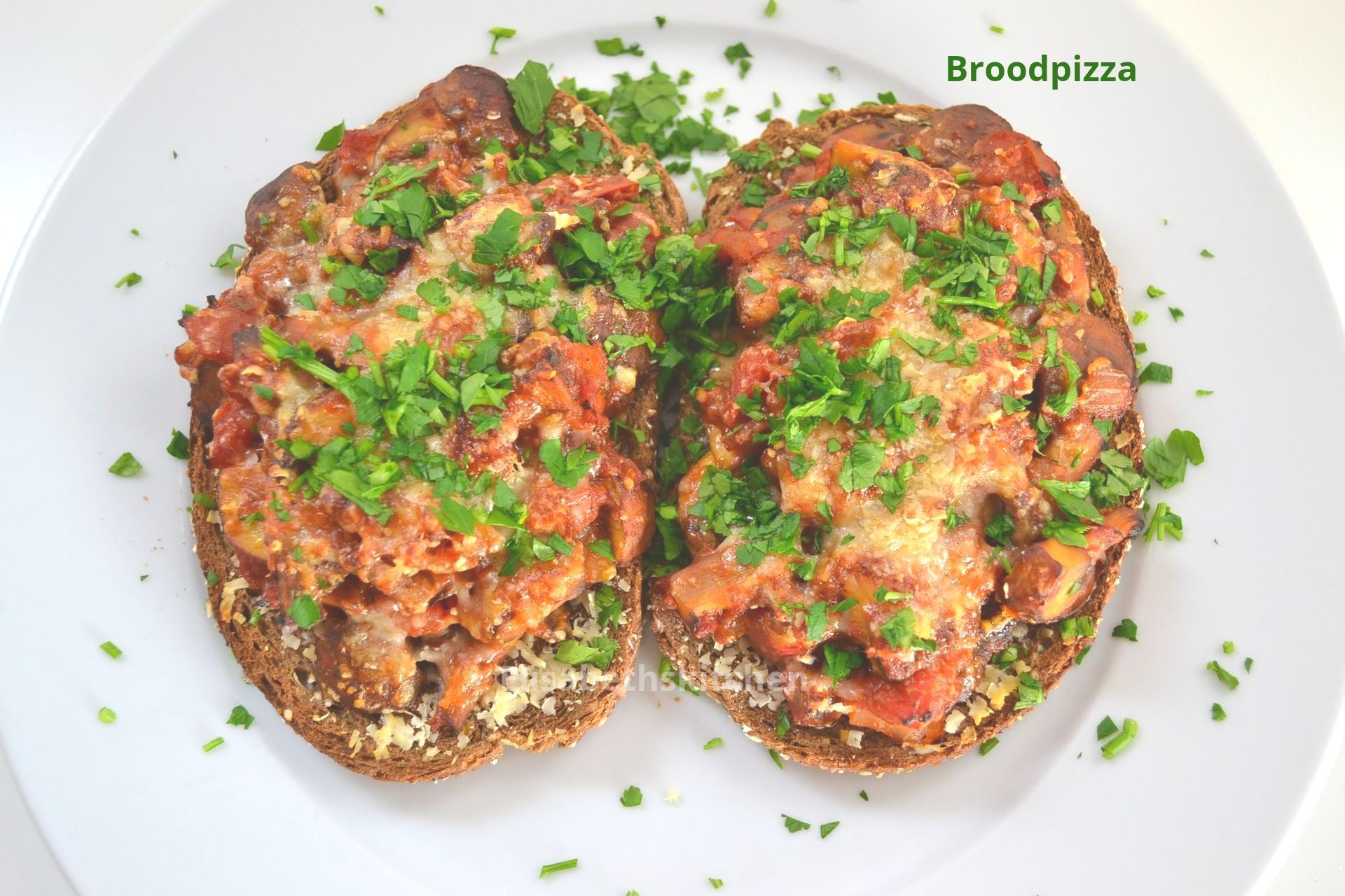 Twee sneetjes brood belegd met een mengsel van tomaat en champignons, kaas en peterselie, op een wit bord.