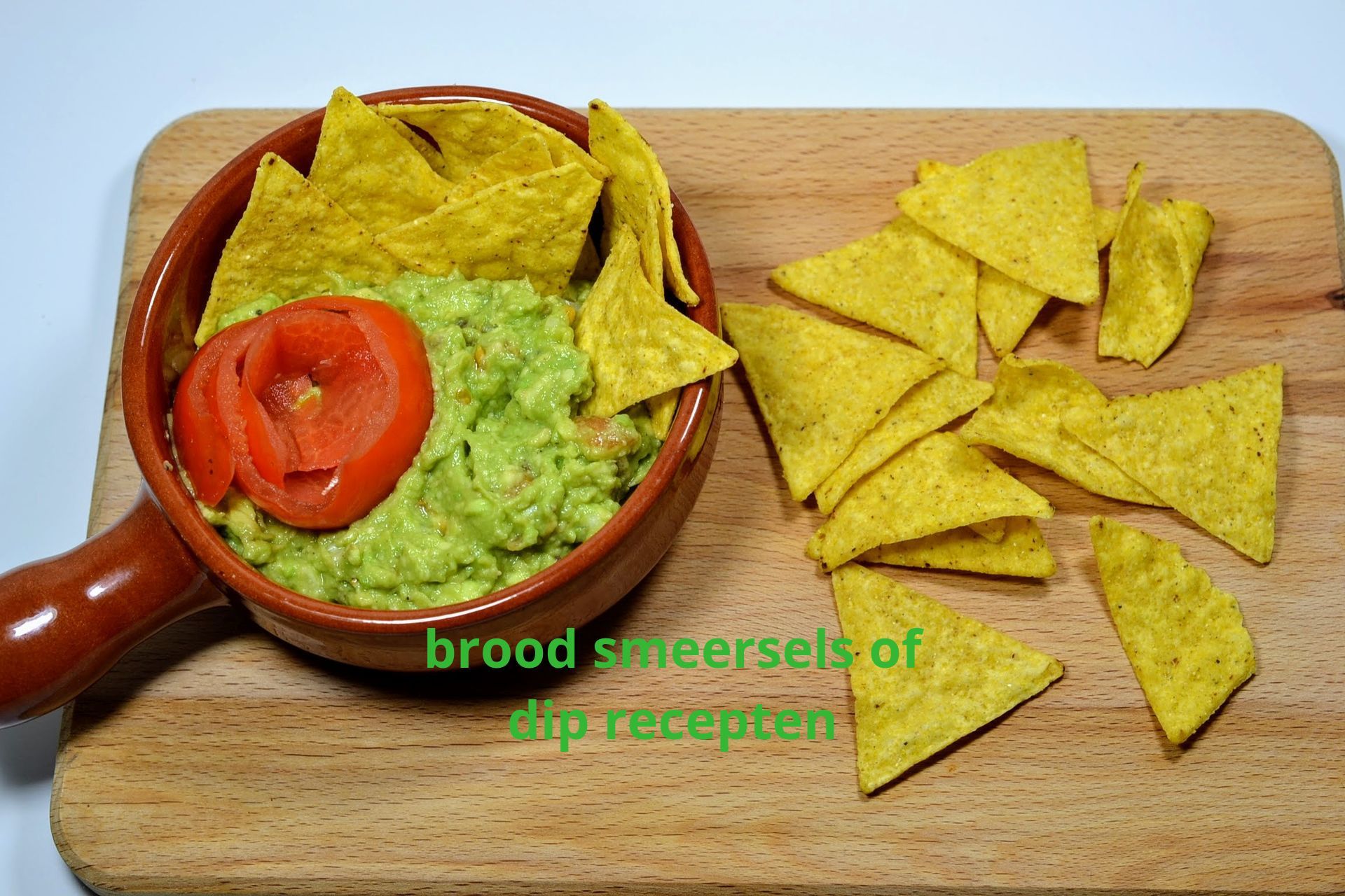 scroll snel verder voor het overzicht en maak je keuze Guacamole in een bruine kom met tortillachips op een houten snijplank; een schijfje tomaat op de guacamole.