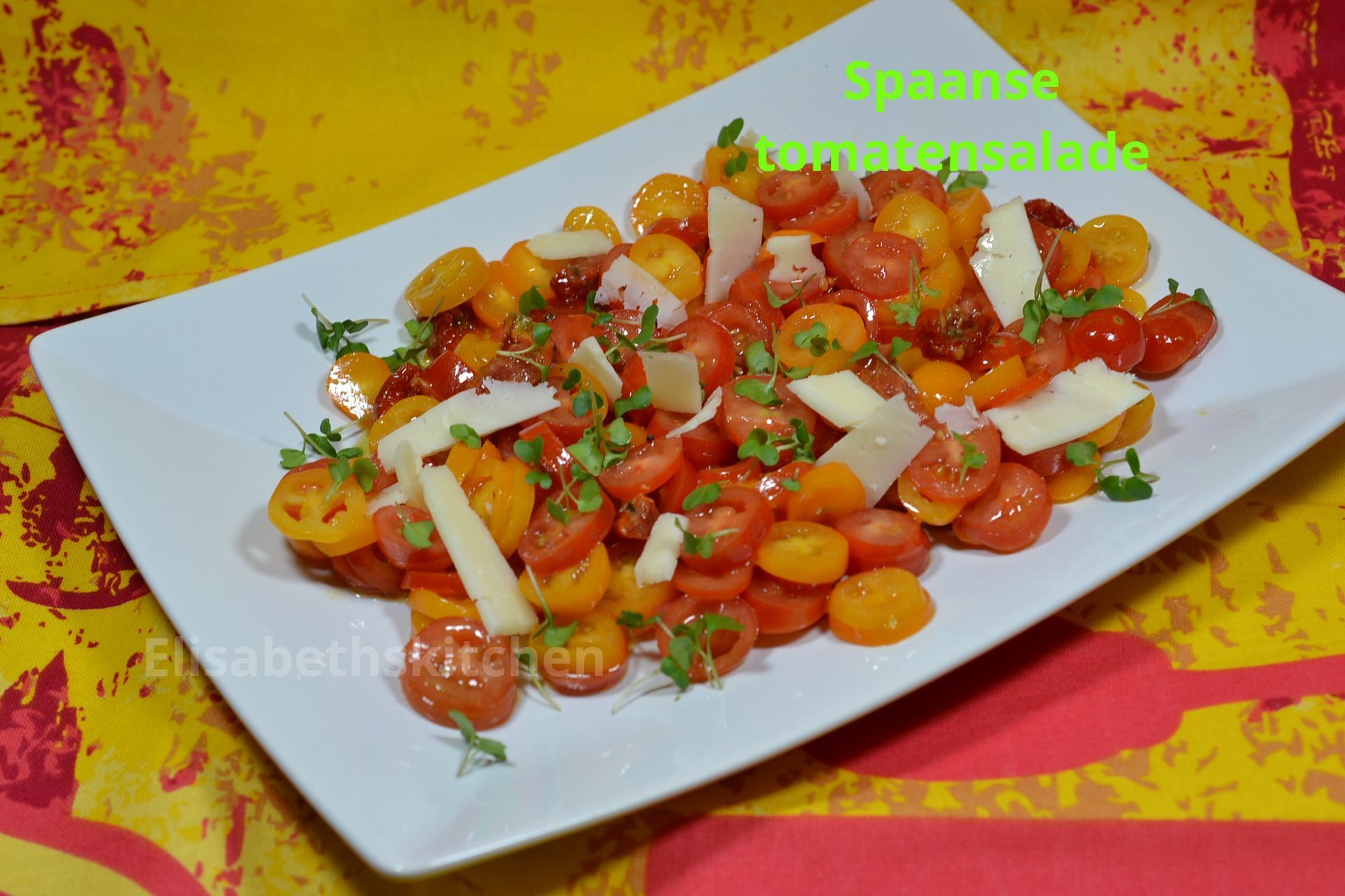 Salade van cherrytomaatjes met geraspte Parmezaanse kaas en kruiden op een wit bord.