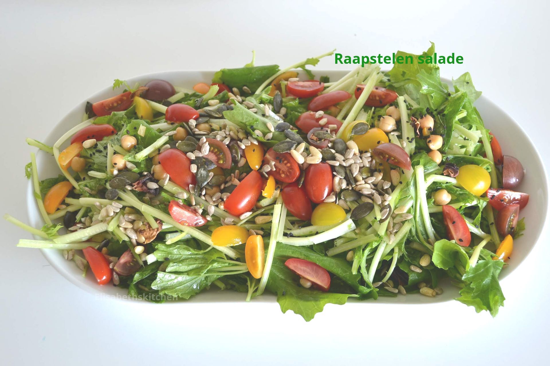 Scroll door voor het recept Salade met gemengde sla, tomaten, kikkererwten en zaden op een wit ovaal bord.