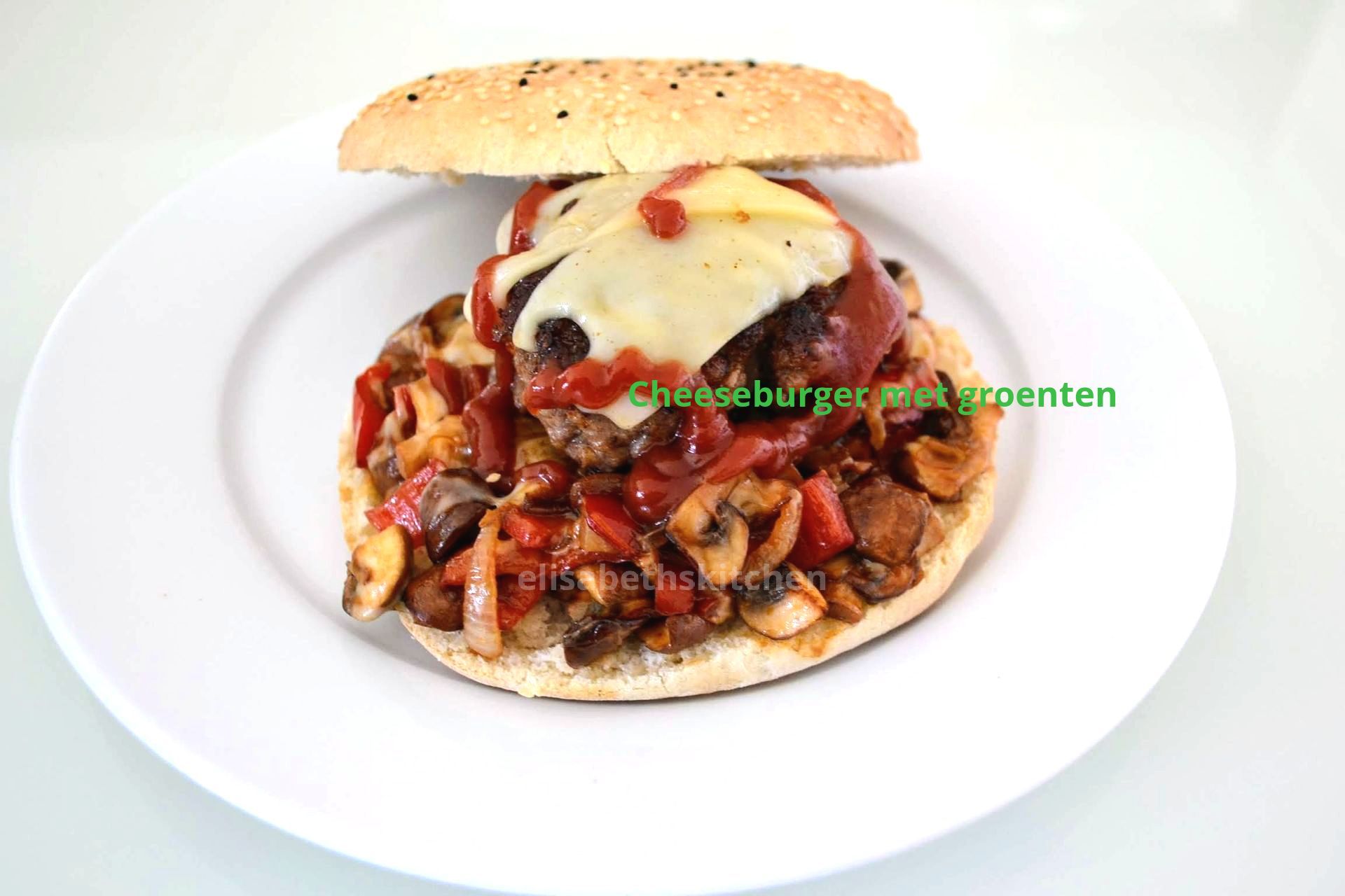 Cheeseburger met kaas, rode saus en groenten, op een broodje, geserveerd op een wit bord.