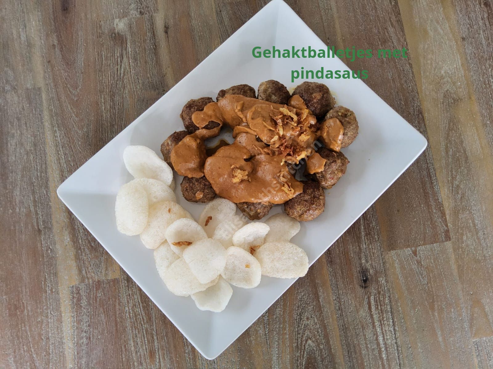 Gehaktballetjes met pindasaus en crackers op een wit bord.