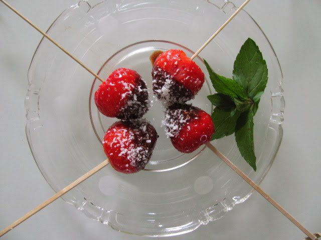 Chocoladeaardbeien aan spiesjes, geserveerd op een glazen bord met een takje munt.