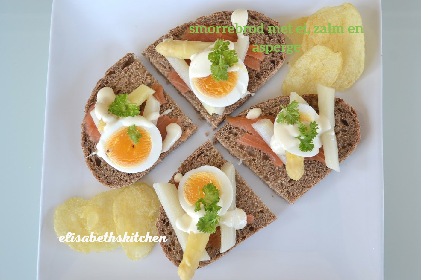 Smørrebrød-sandwiches met zalm, ei, asperges en friet op een wit bord.