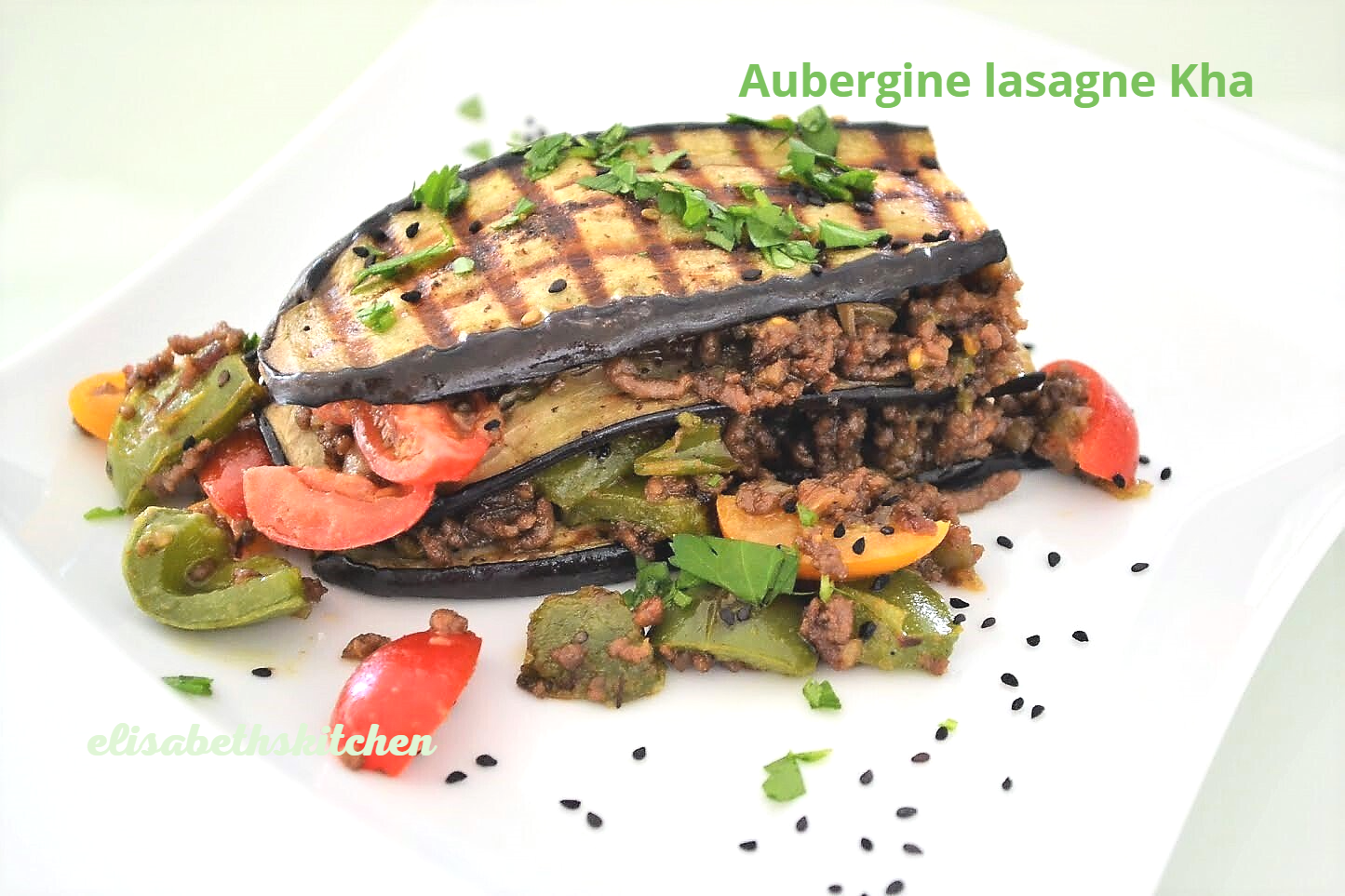 Auberginelasagne met gegrilde aubergine, vleesvulling en groenten op een wit bord.