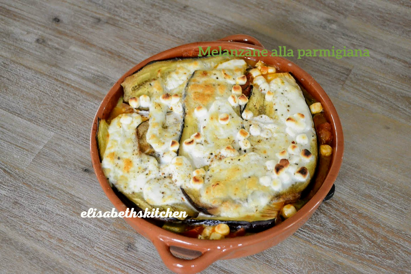 Aubergineparmesan in een terracotta schaal, bedekt met gesmolten mozzarella, gebakken op een houten ondergrond.