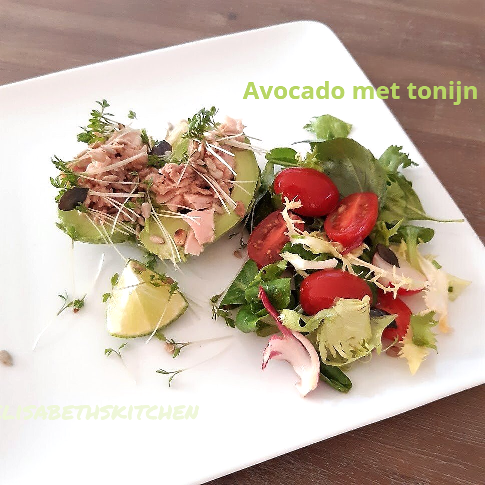Gehalveerde avocado's gevuld met tonijn, salade, tomaten en limoen op een wit bord.