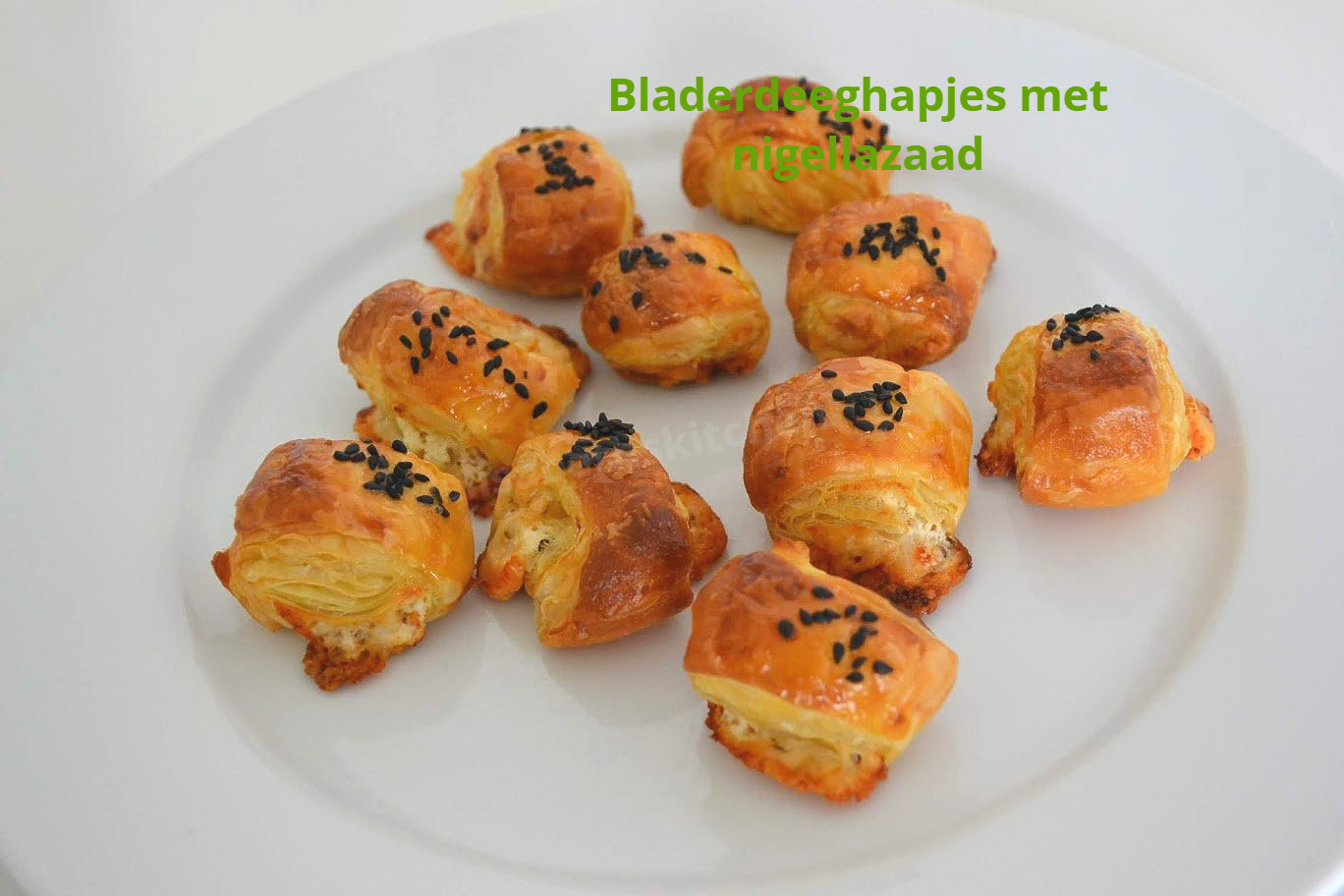 Gouden bladerdeeghapjes met zwarte sesamzaadjes, geserveerd op een wit bord.