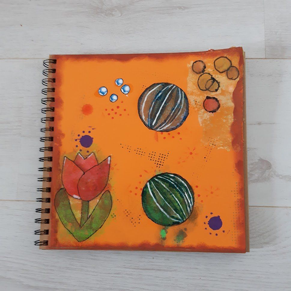 Oranje schetsboek met kleurrijke abstracte illustraties van bloemen en ballen.