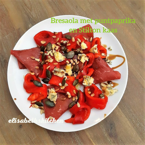 Bresaola met rode paprika en Stiltonkaas op een wit bord, bestrooid met zaden.