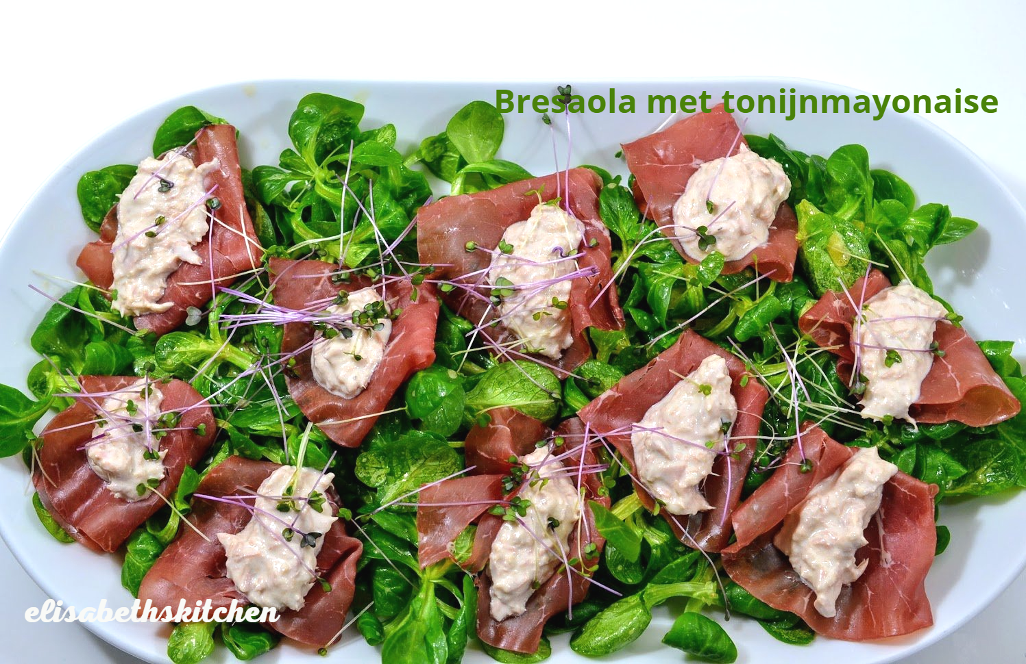 Bresaola met tonijnmayonaise op een bedje van groene bladgroenten, gegarneerd met taugé, op een wit bord.