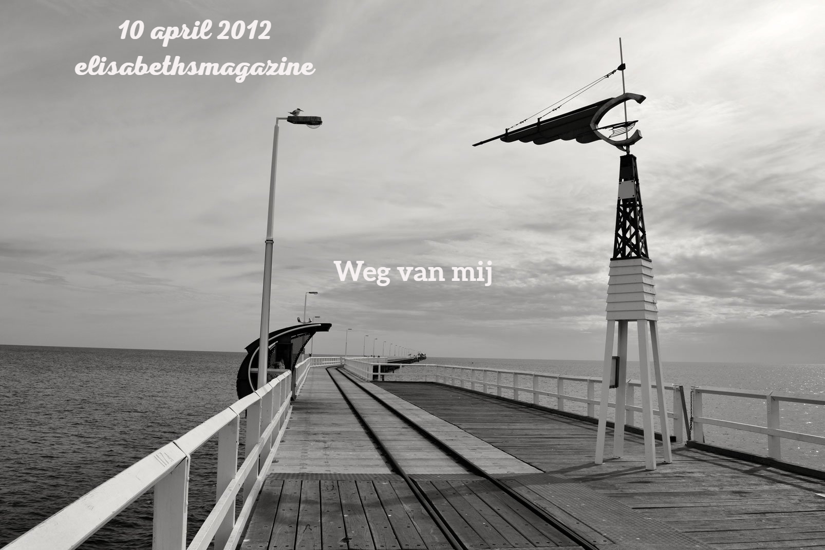 Een zwart-witte pier steekt de oceaan in, met een navigatietoren en een bewolkte hemel.
