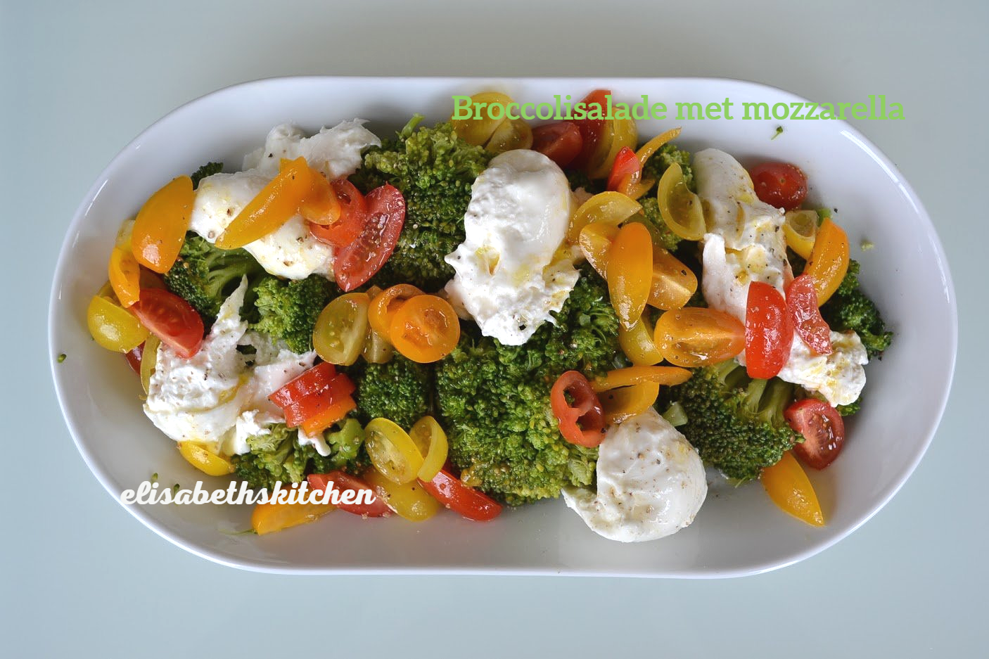 Broccolisalade met mozzarella, gele en rode tomaten in een witte ovale schaal.