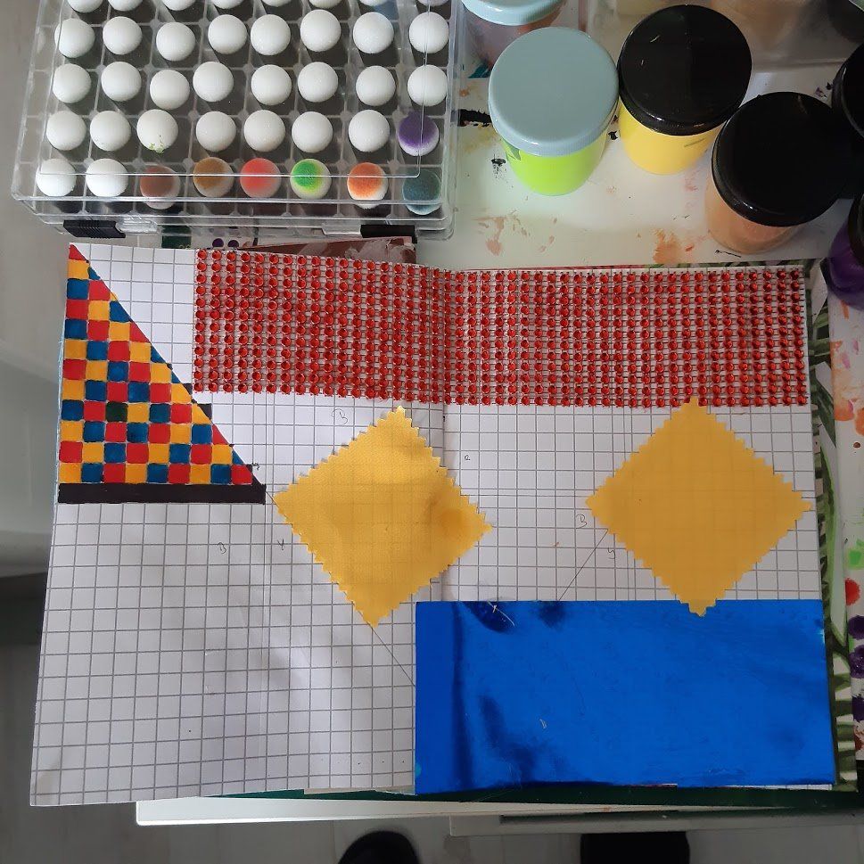 Teken- en schildermaterialen en papier met geometrische patronen en gekleurde vierkantjes.