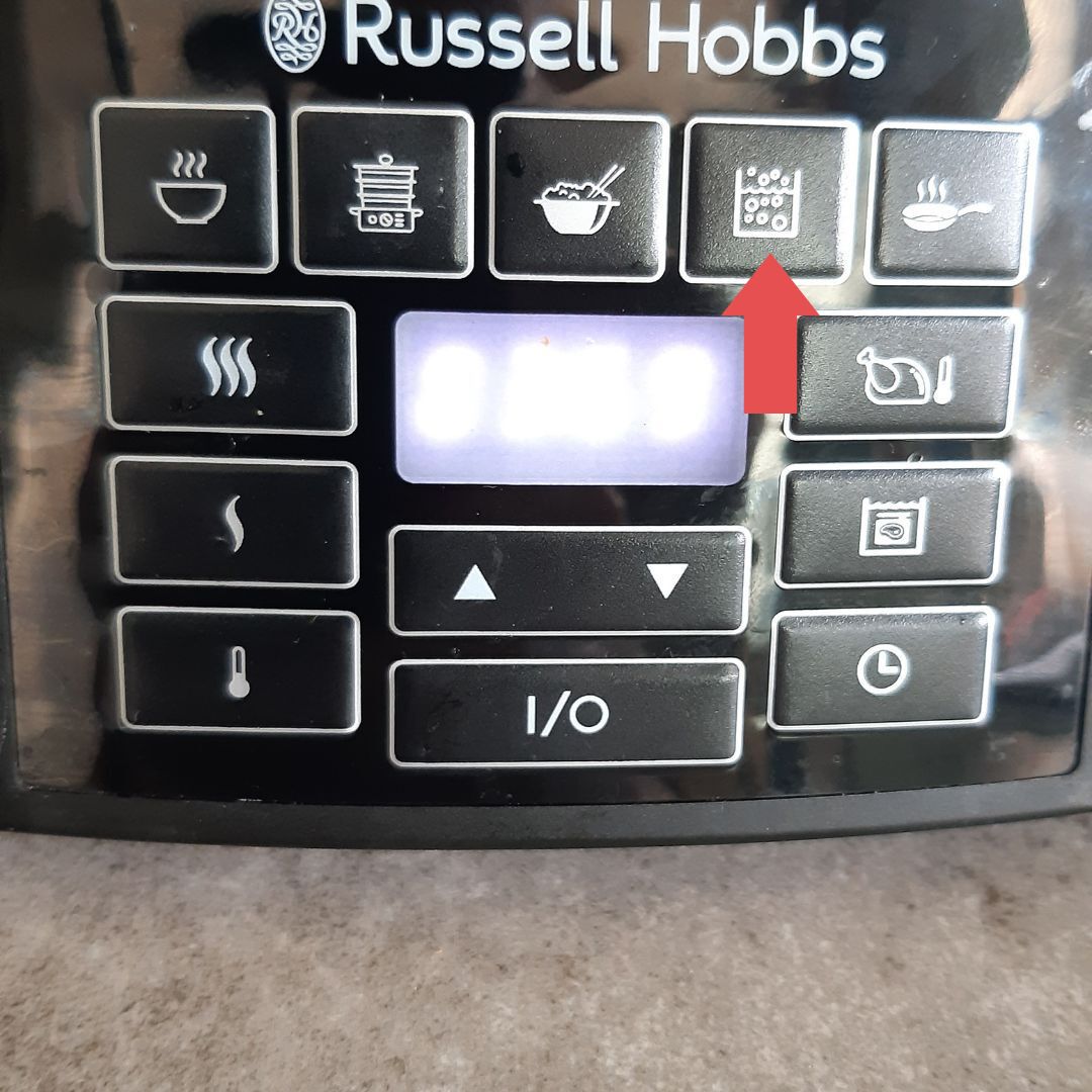 Detailopname van een bedieningspaneel van een Russell Hobbs-apparaat; de rode pijl wijst naar een knop met een raster van vierkantjes.