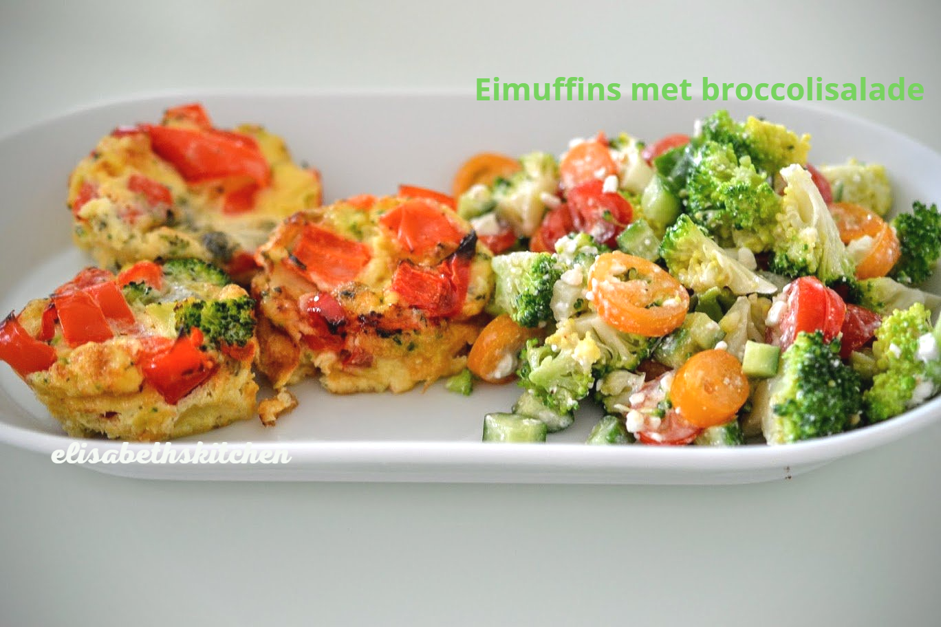 Eimuffins met rode tomaten en broccolisalade op een wit bord.