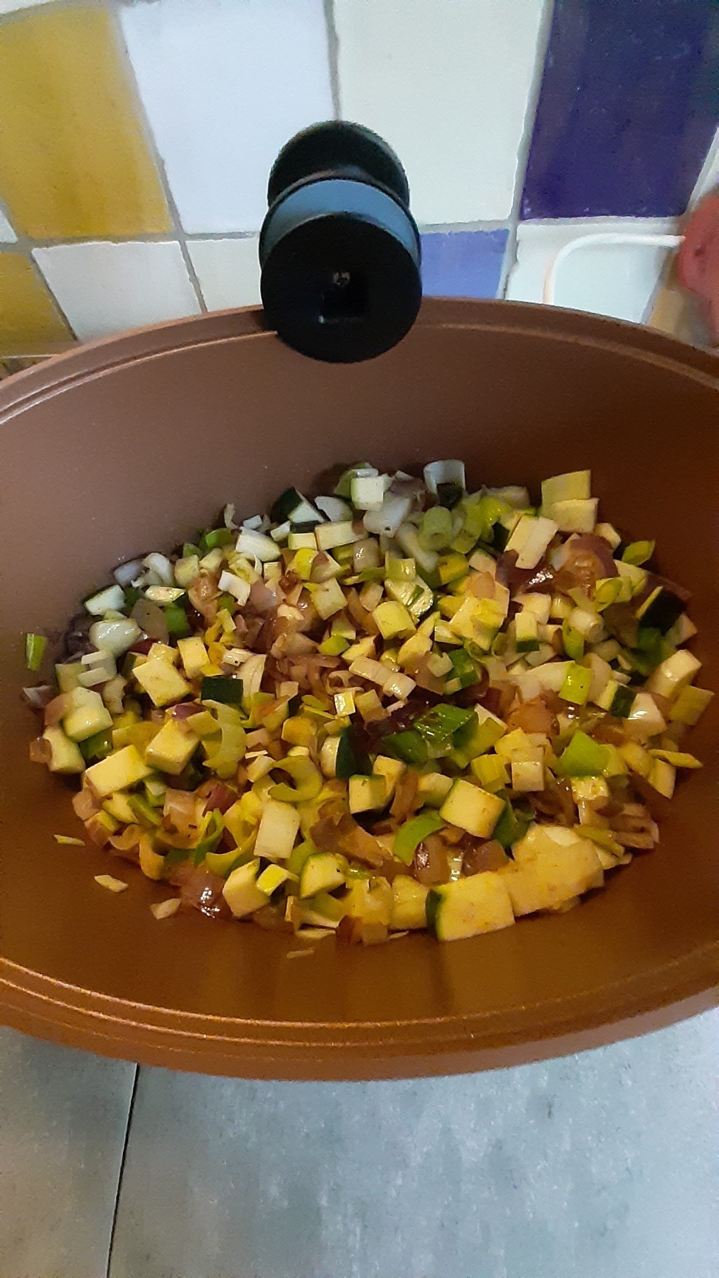 Gesneden groenten in een bruine kom, waaronder courgette en prei, met een pepermolen erbovenop.