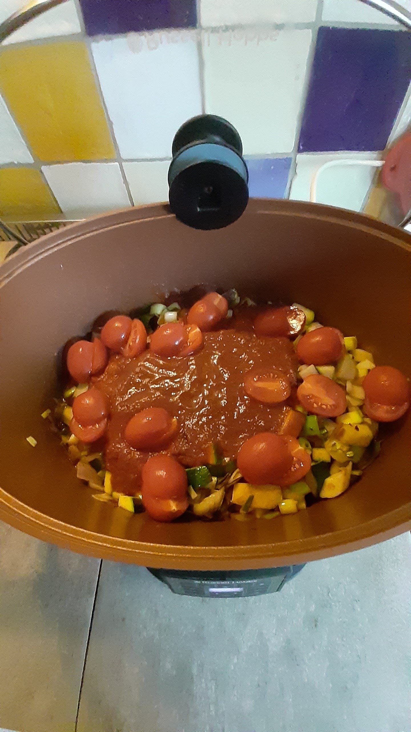 Slowcooker met groenten, saus en cherrytomaten; deksel open.