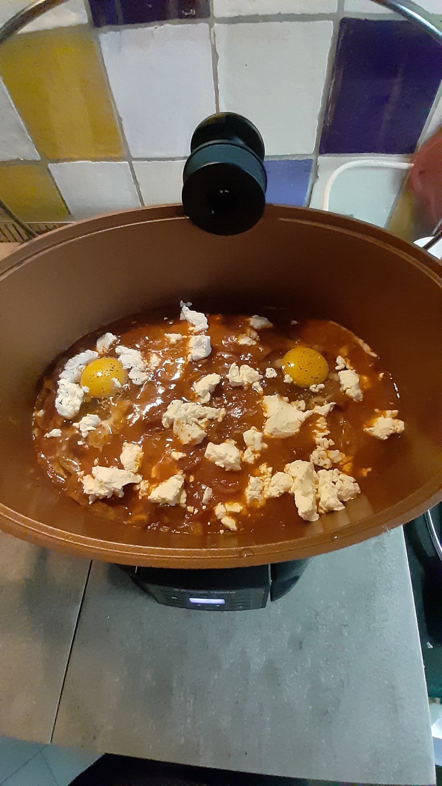 Eieren in een pan met rode saus en kaas; pan op het fornuis.