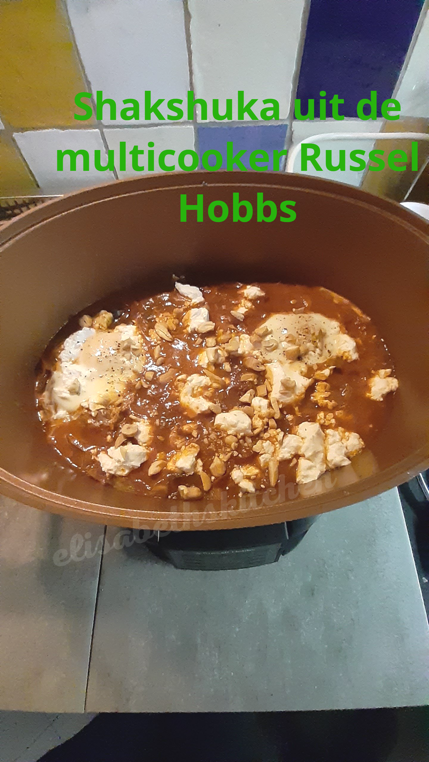 Shakshuka bereid in een bruine multicooker op het fornuis, gegarneerd met verkruimelde witte kaas en donkere saus.