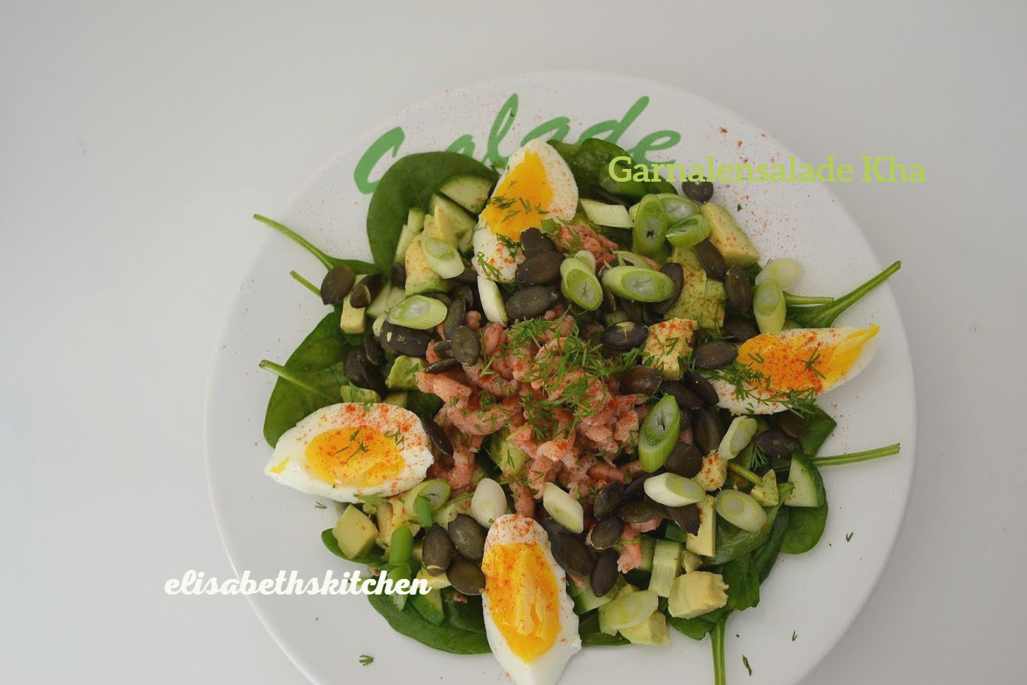 Salade op een wit bord met spinazie, avocado, eieren en zaden.