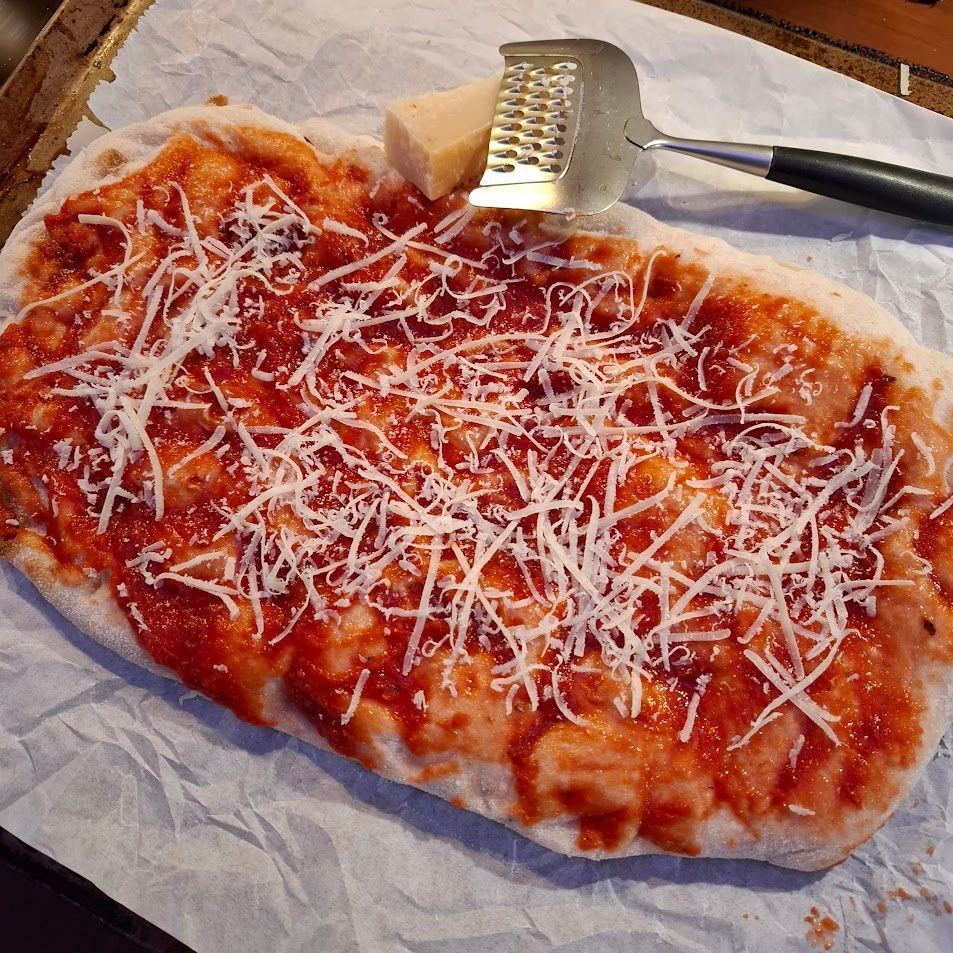 Pizza met rode saus en geraspte kaas, met kaasrasp en kaasblok.