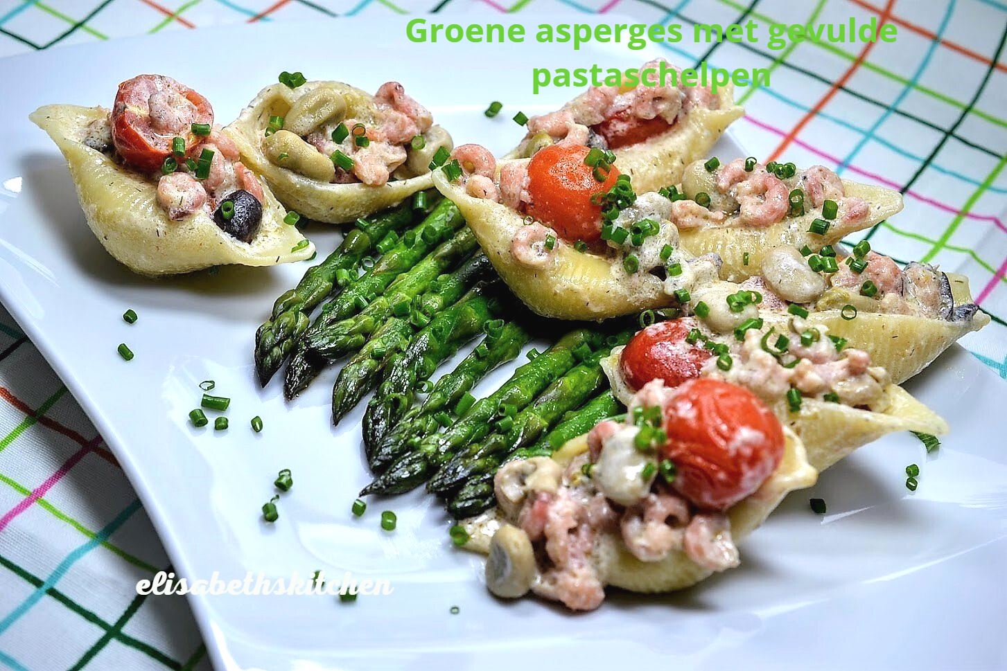 Een bord pastaschelpjes met garnalen, tomaten en asperges.