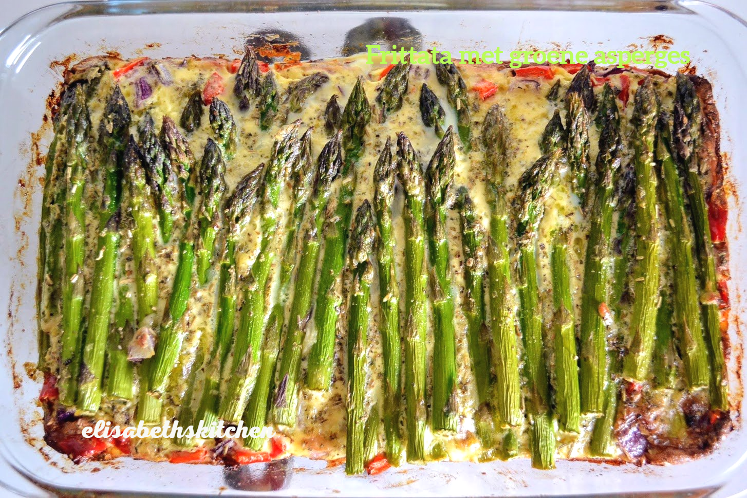 Gebakken asperges met romige saus in een glazen schaal. Groene asperges, witte saus en rode paprika.