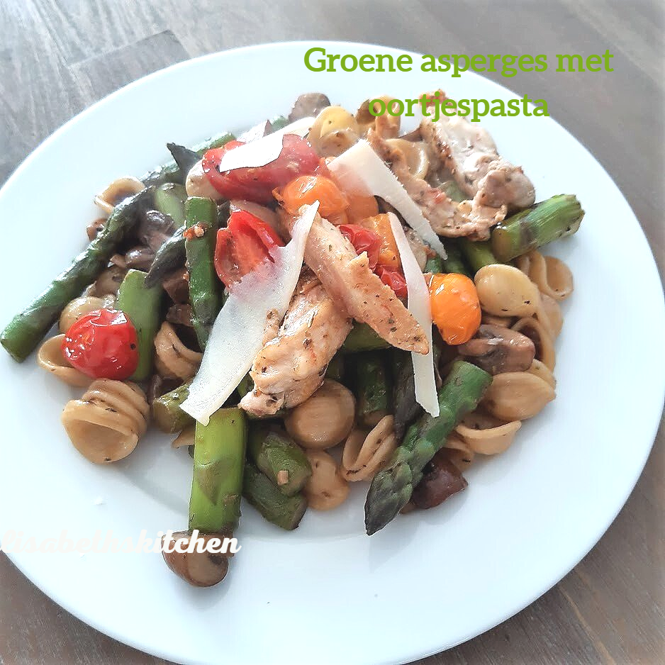 Pastagerecht met groene asperges, cherrytomaten, kip en geraspte Parmezaanse kaas op een wit bord.