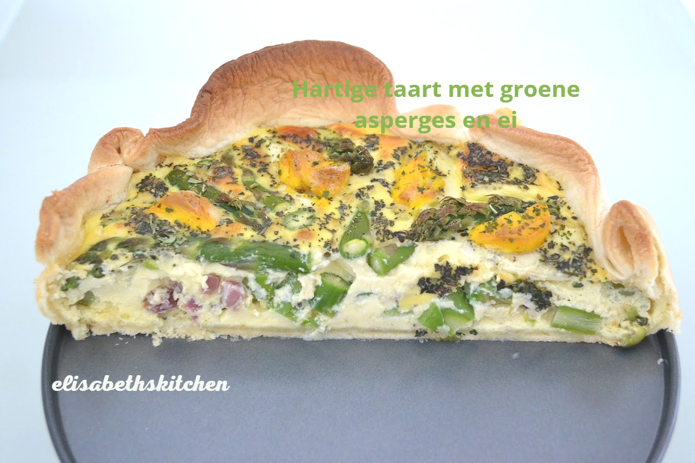 Quiche met groene asperges en ei, lichtgroene vulling, gebakken korst, op een grijs bord.