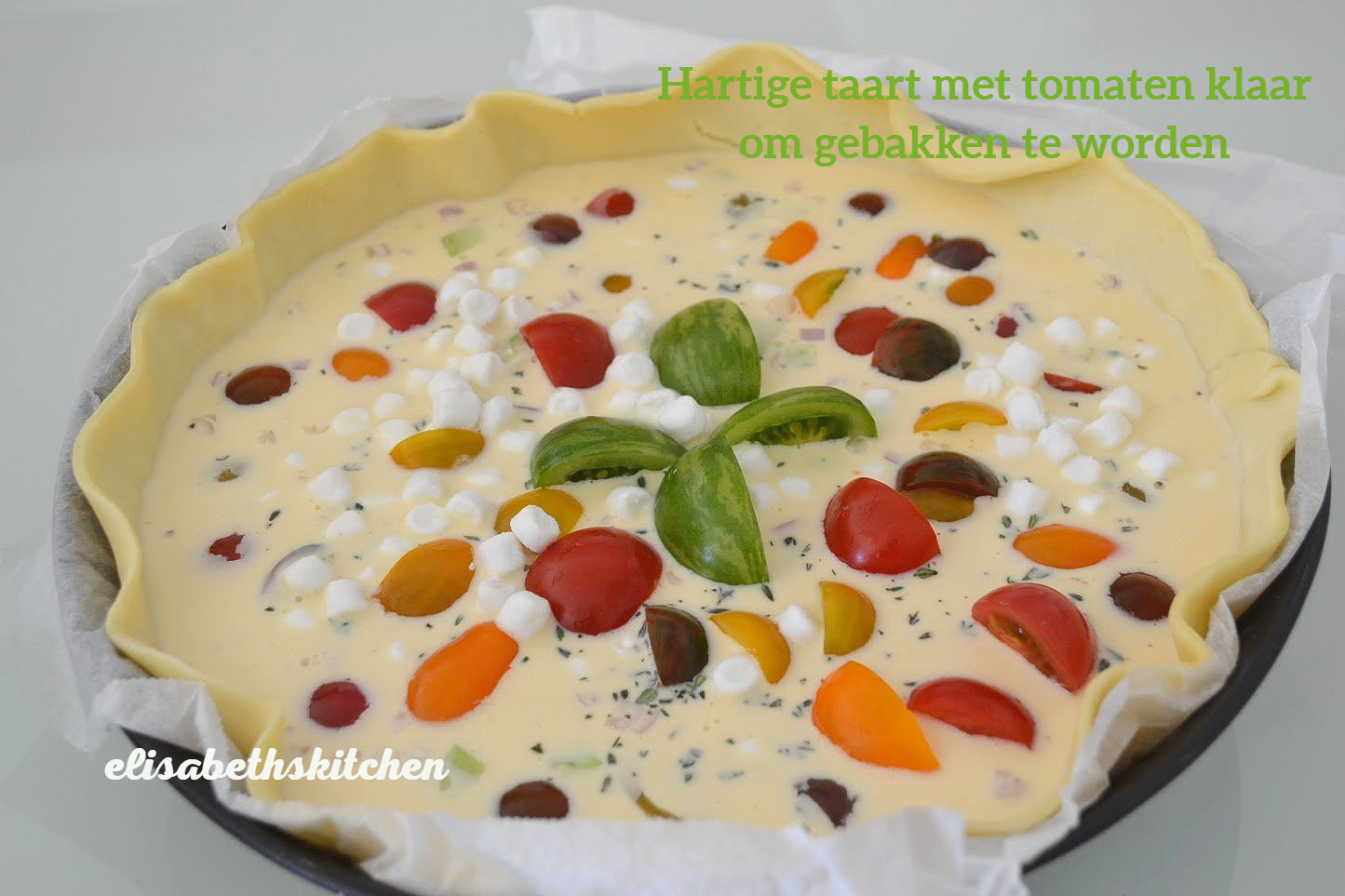 Tomatentaart in een ovenschaal, gevuld met tomaten, kaas en kruiden, klaar om te bakken.