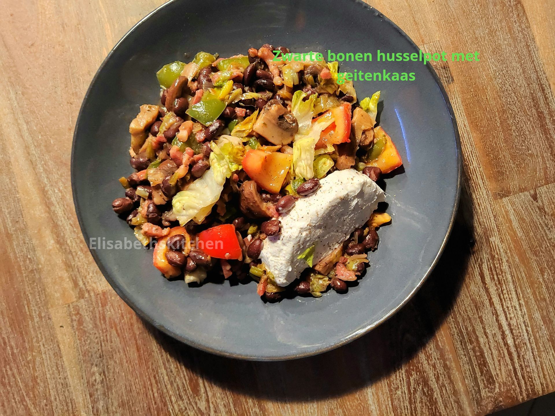 Een gerecht van zwarte bonen en groenten met een klodder witte kaas in een grijze kom op een houten tafel.