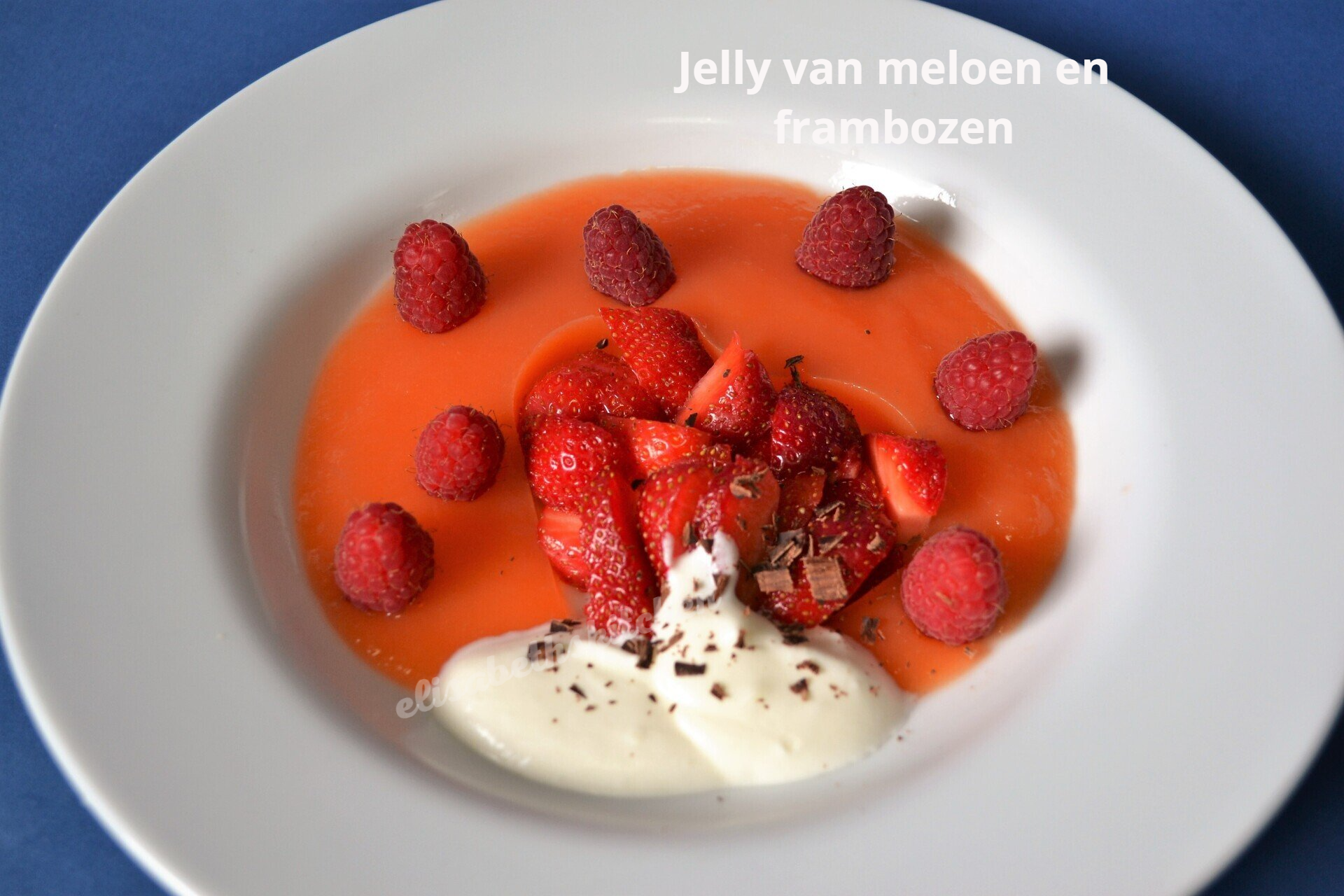 Wit bord met roze gelei, aardbeien, frambozen en slagroom, afgewerkt met chocoladeschaafsel.