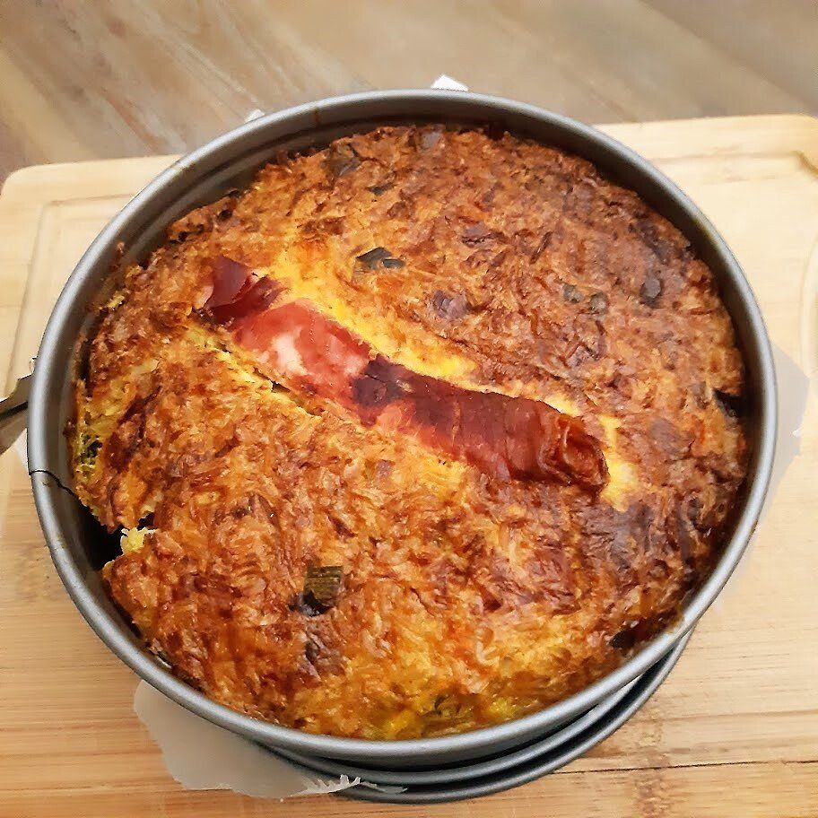 Hartige quiche in een ronde metalen vorm, met een goudbruine korst en een plak ham.