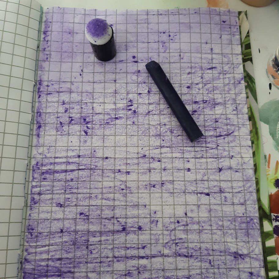 Paars kleurpotlood en inkt op een notitieboekje met ruitjespapier. Het kleurpotlood is een cilindervormig staafje.