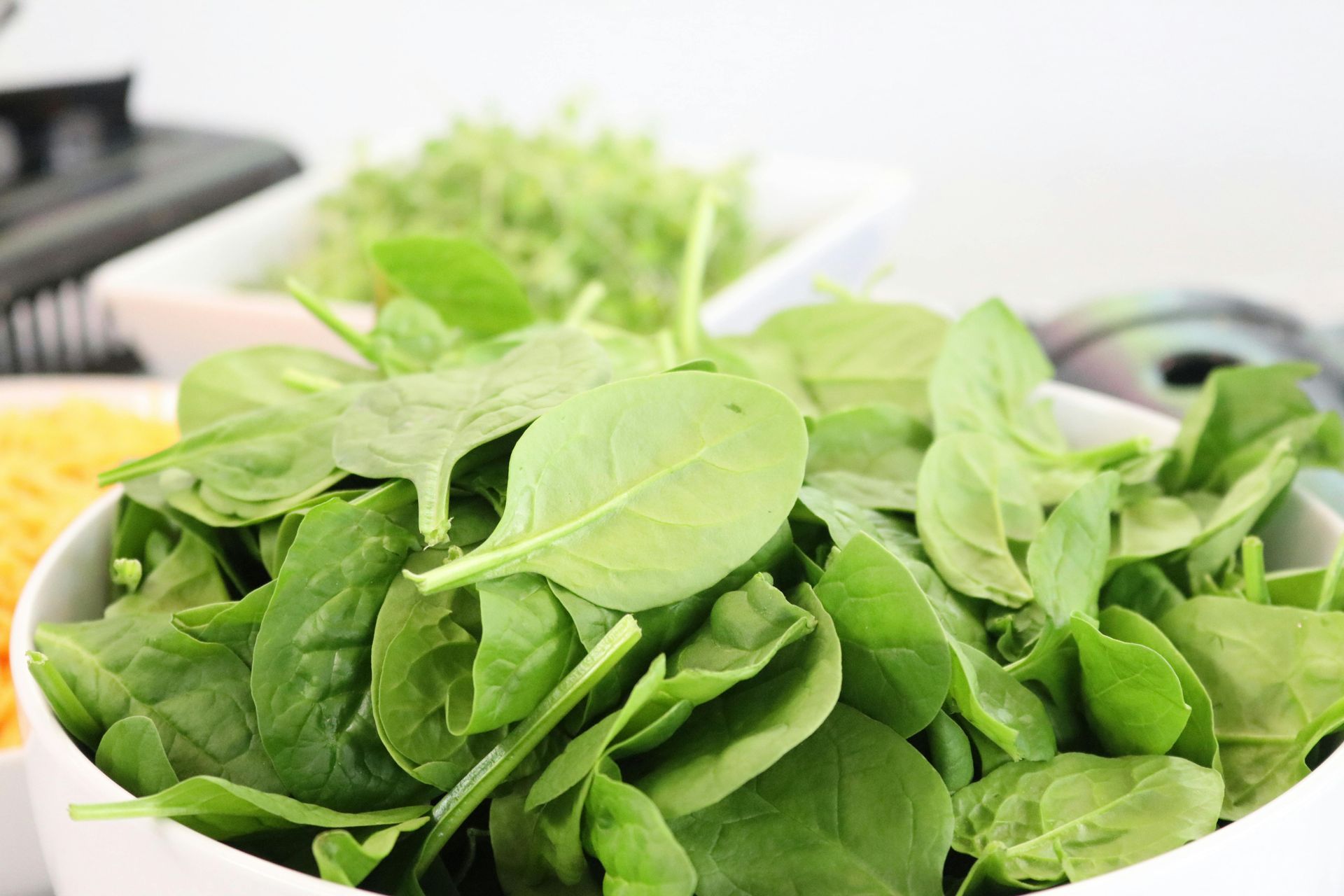 Een kom met verse, groene spinazieblaadjes, in een keukensetting met andere ingrediënten op de achtergrond.