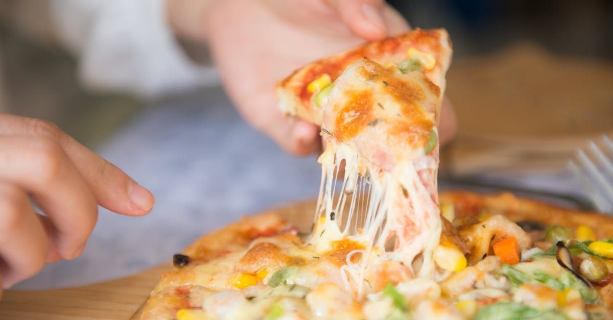 Een persoon houdt een stuk pizza vast, met gesmolten kaas die zich naar de pizza uitstrekt.