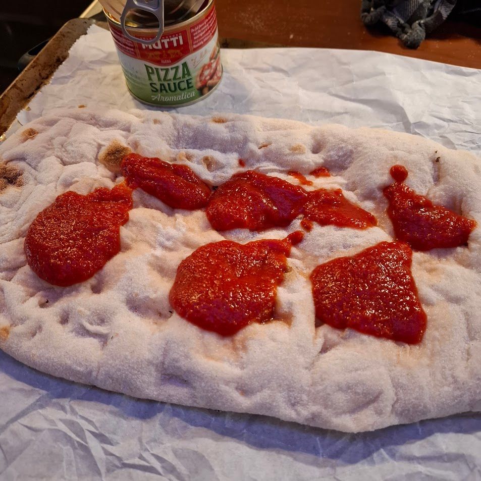 Pizzabodem met klodders rode pizzasaus en een blik pizzasaus.