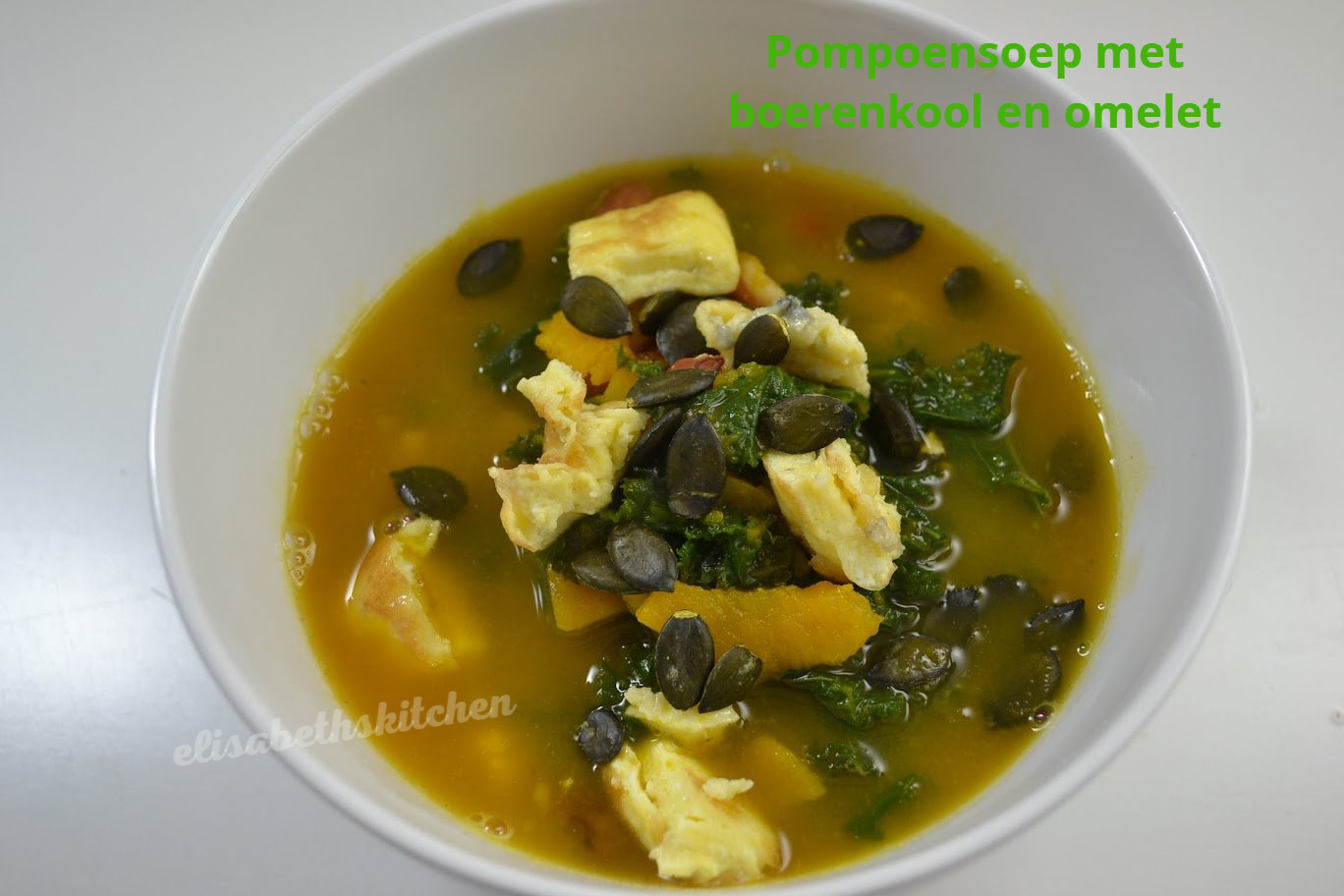 Pompoensoep met boerenkool en omelet, gegarneerd met pompoenpitten, geserveerd in een witte kom.