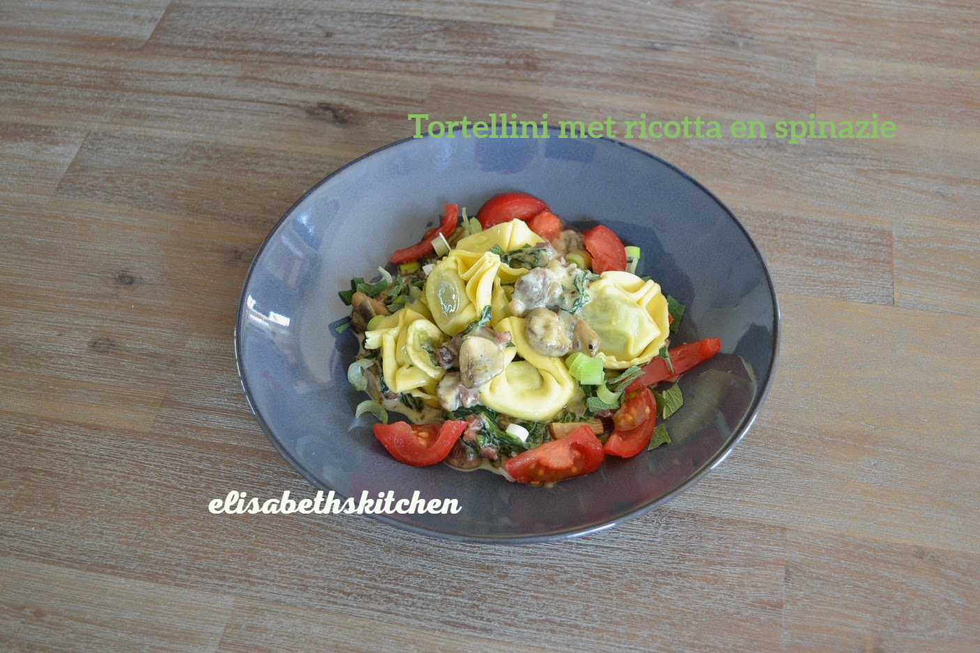 Tortellini met ricotta en spinazie in een kom met tomaten en groene bladgroenten.