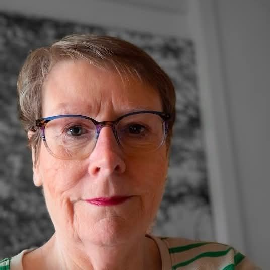 Vrouw met bril, gekleed in een gestreept shirt, kijkt met een neutrale uitdrukking in de camera.