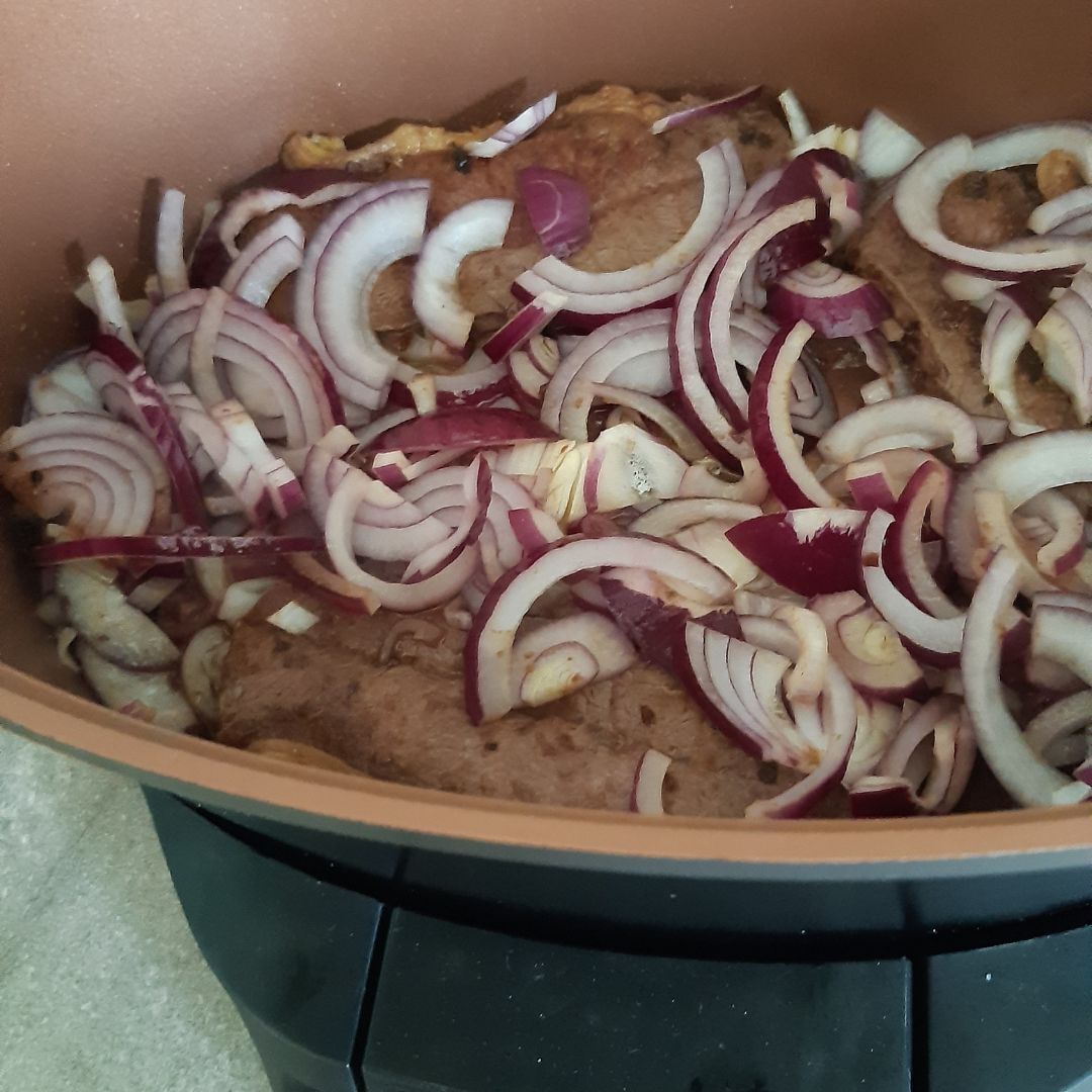 Varkenskarbonades en gesneden rode uien worden gebakken in een bruine pan op een zwart fornuis.