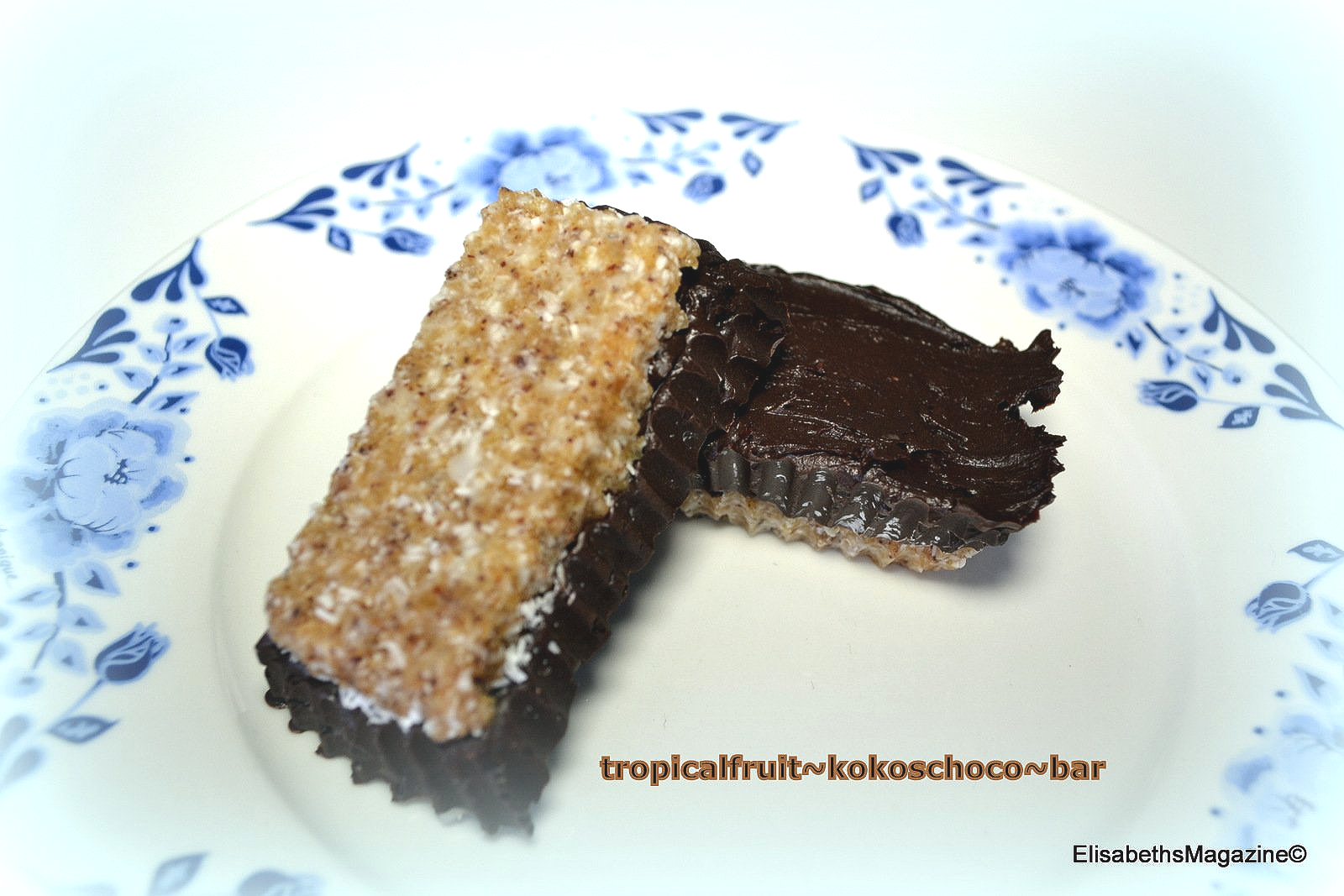 Een chocoladereep met tropisch fruit op een bord met bloemmotief. De reep is doorgesneden, waardoor de vulling zichtbaar is.