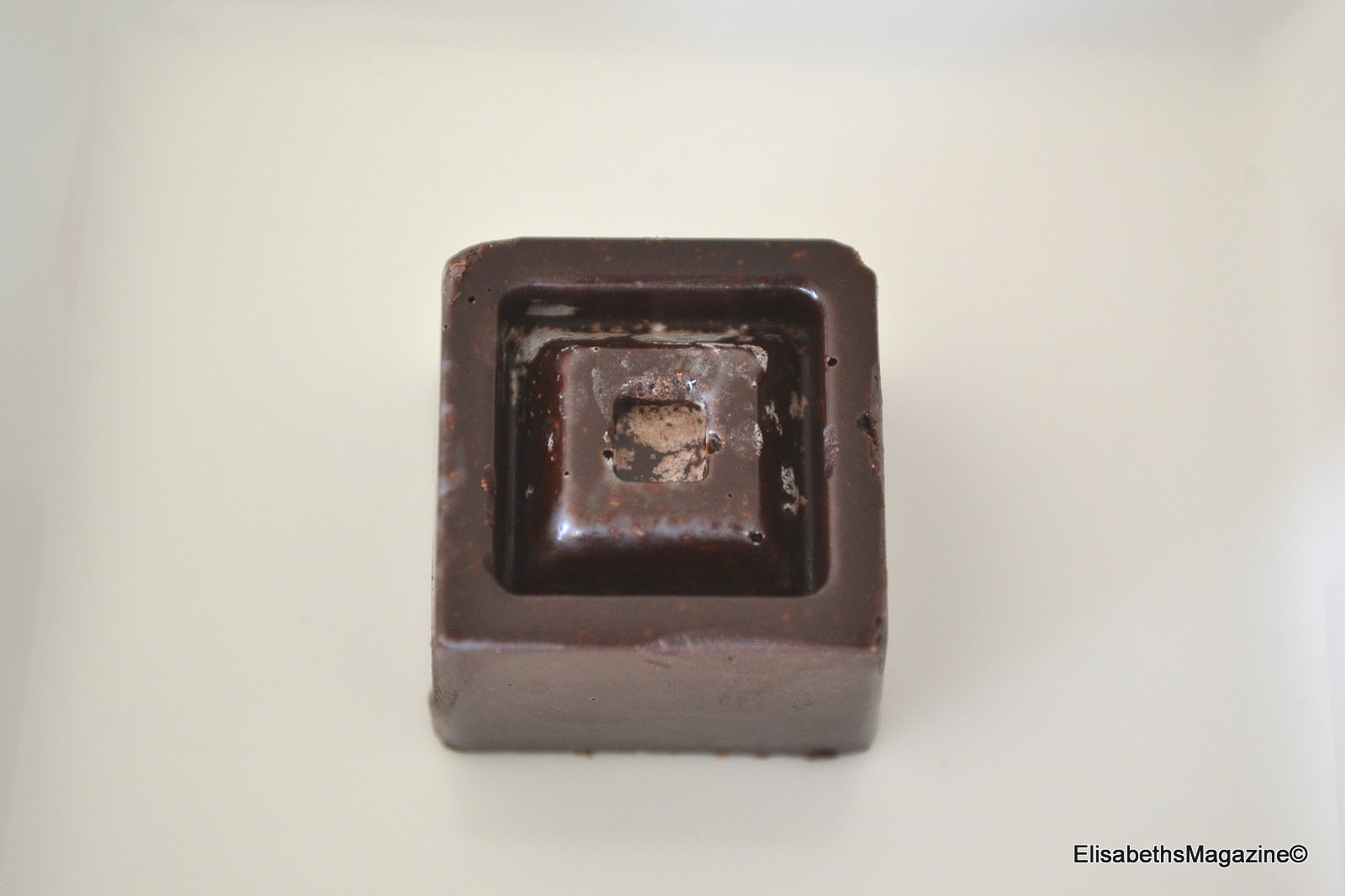 Donkerbruine vierkante chocolade met een verzonken midden op een wit bord.