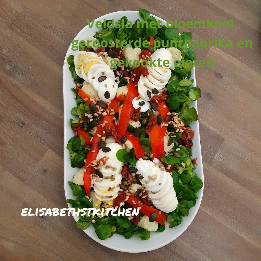 Salade met bloemkool, geroosterde paprika en gekookte eieren op een wit bord.