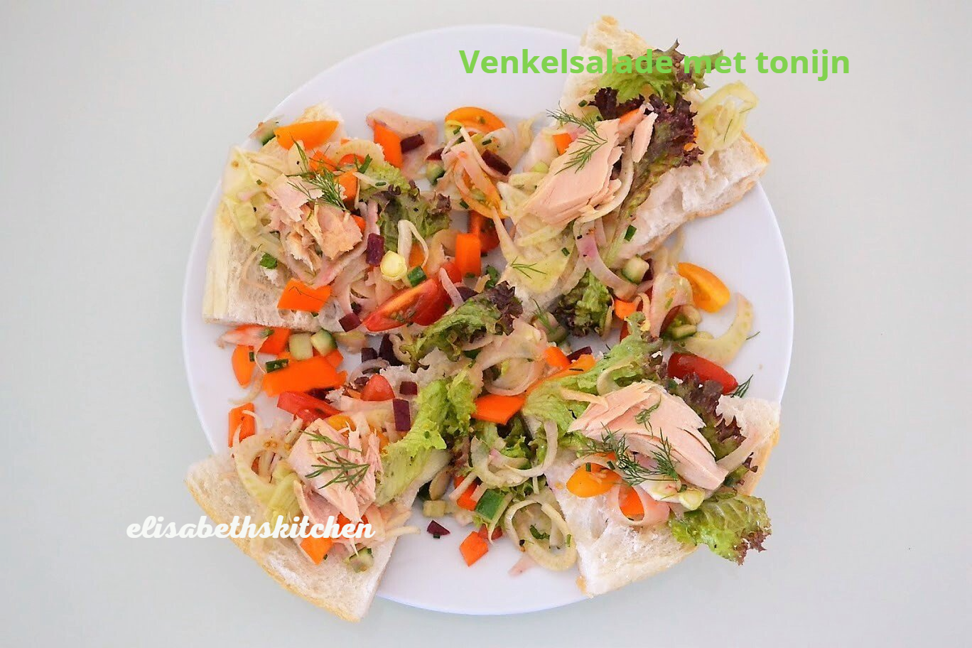 Salade met vis, kleurrijke groenten en sneetjes brood op een wit bord.
