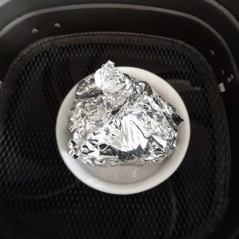 Een kom met voedsel, verpakt in aluminiumfolie, staat in het mandje van een airfryer.